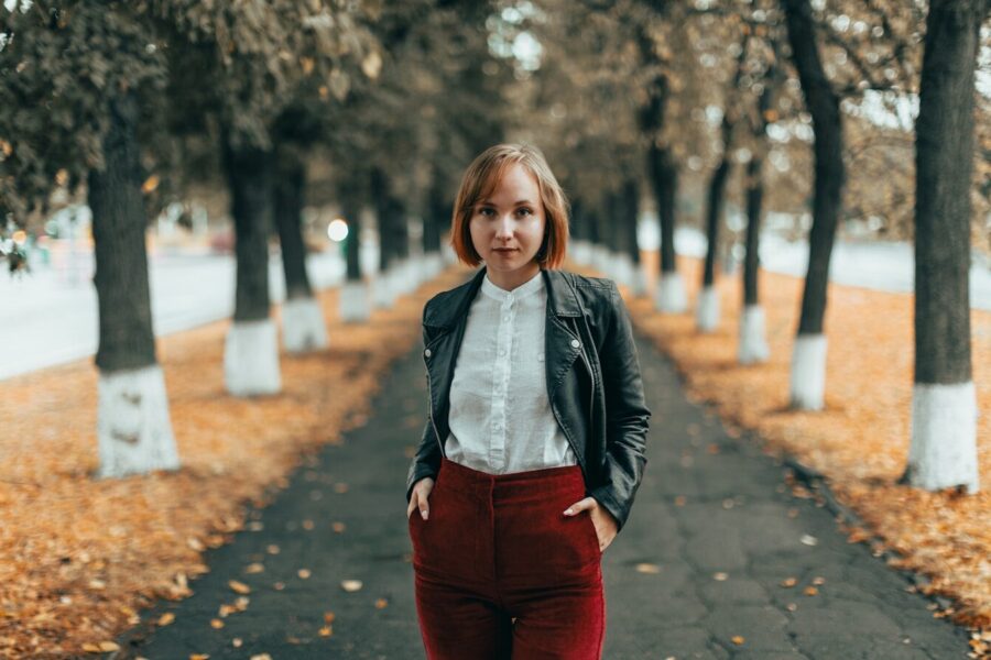 Young woman with adverse childhood experiences standing on autumn path with trees