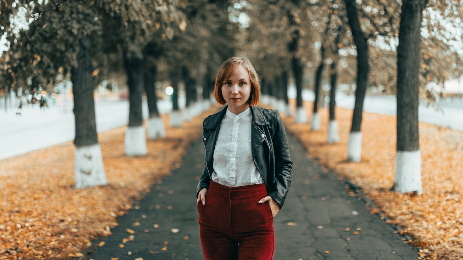 Young woman with adverse childhood experiences standing on autumn path with trees